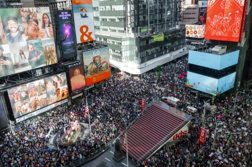 Vista aérea da Times Square, em Nova York, tomada por uma grande multidão de manifestantes com cartazes, cercada por prédios e painéis publicitários.