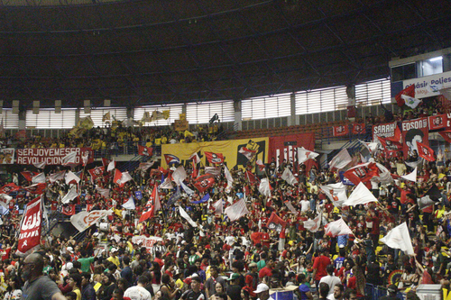 Ginásio lotado de participantes durante plenária do Congresso da UBES. A multidão ocupa arquibancadas e a área central, com diversas bandeiras, faixas e cartazes de movimentos estudantis.